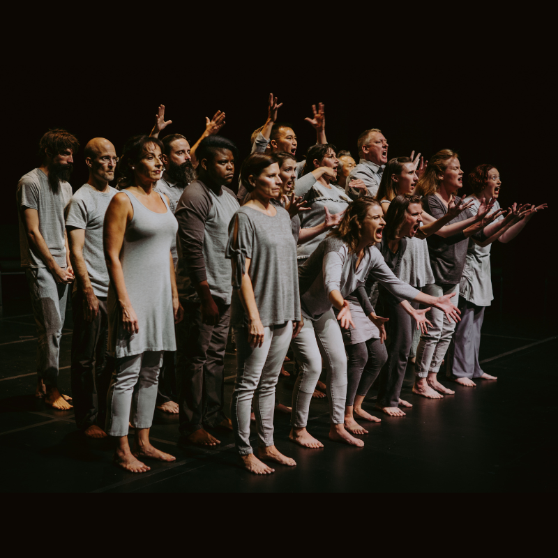A group of people all wearing grey make exasperated expressions onstage.
