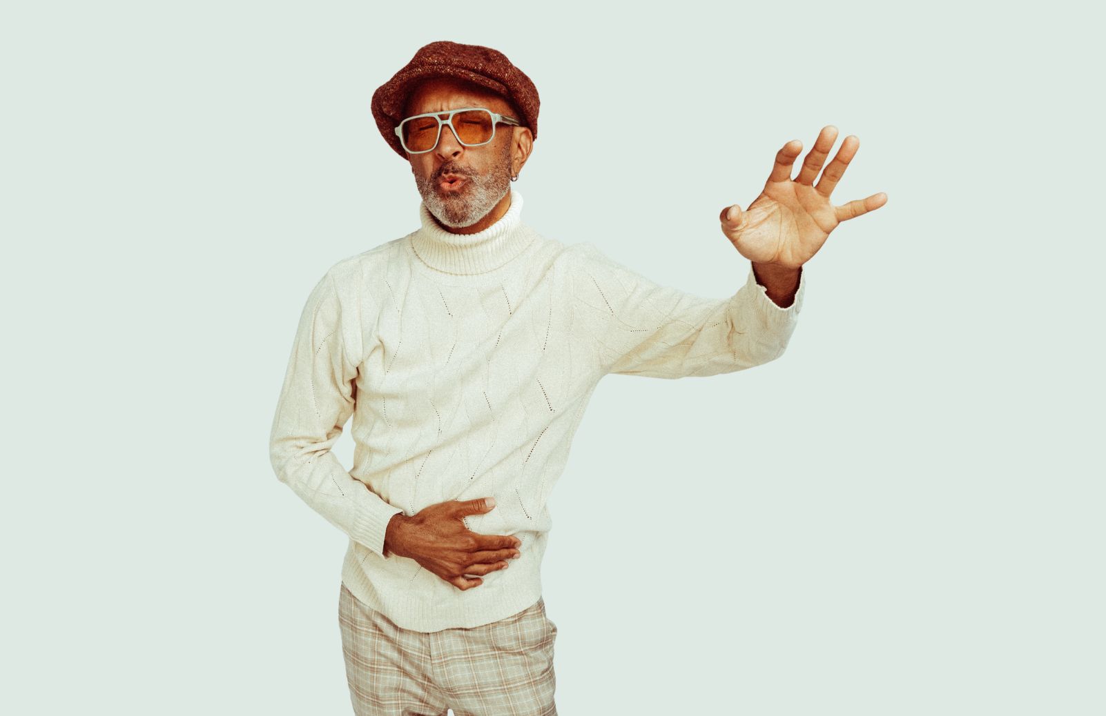 A man in a white shirt and brown hat dances in front of a white backdrop.