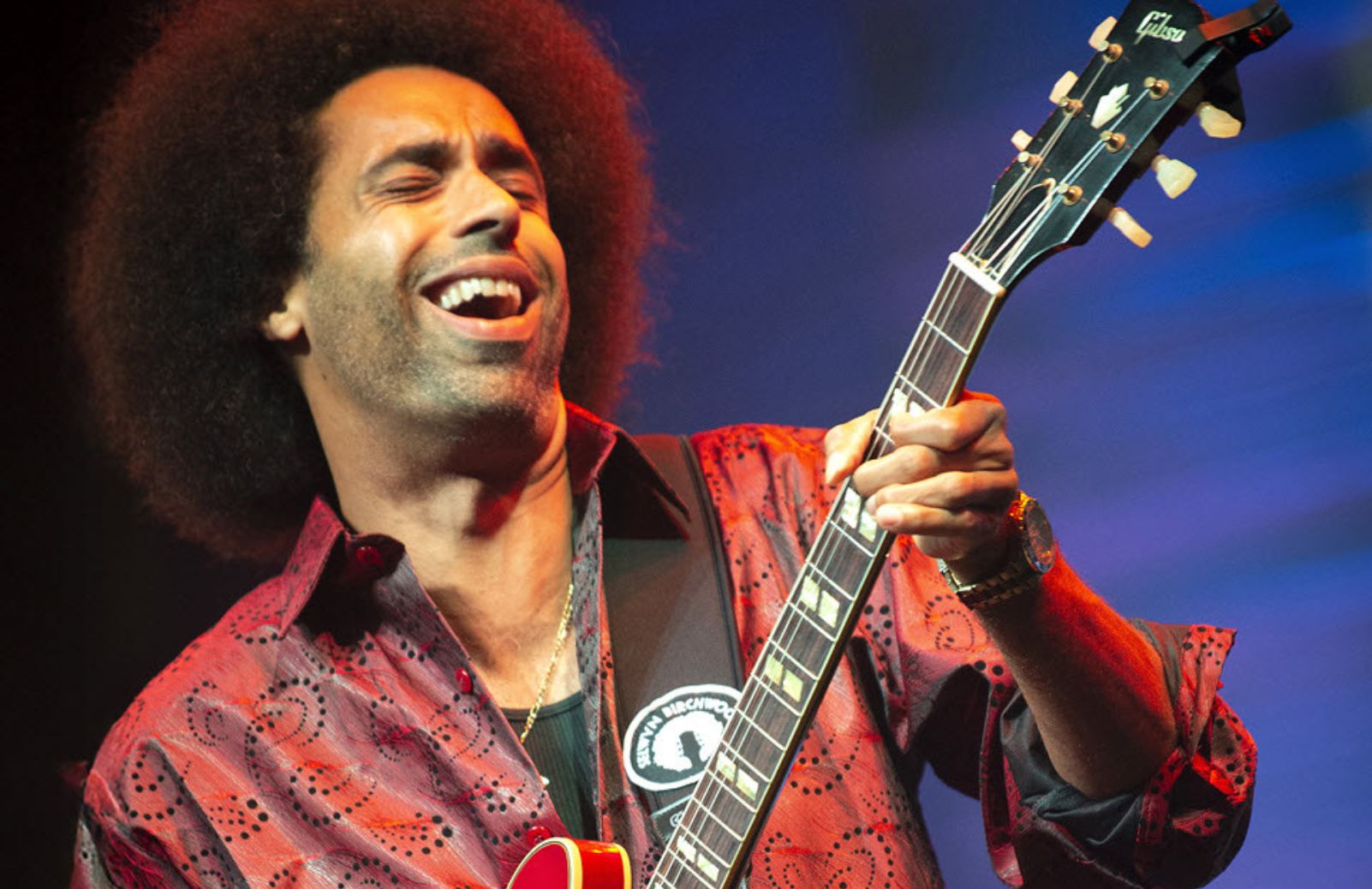 A guitarist laughs while playing an electric guitar.