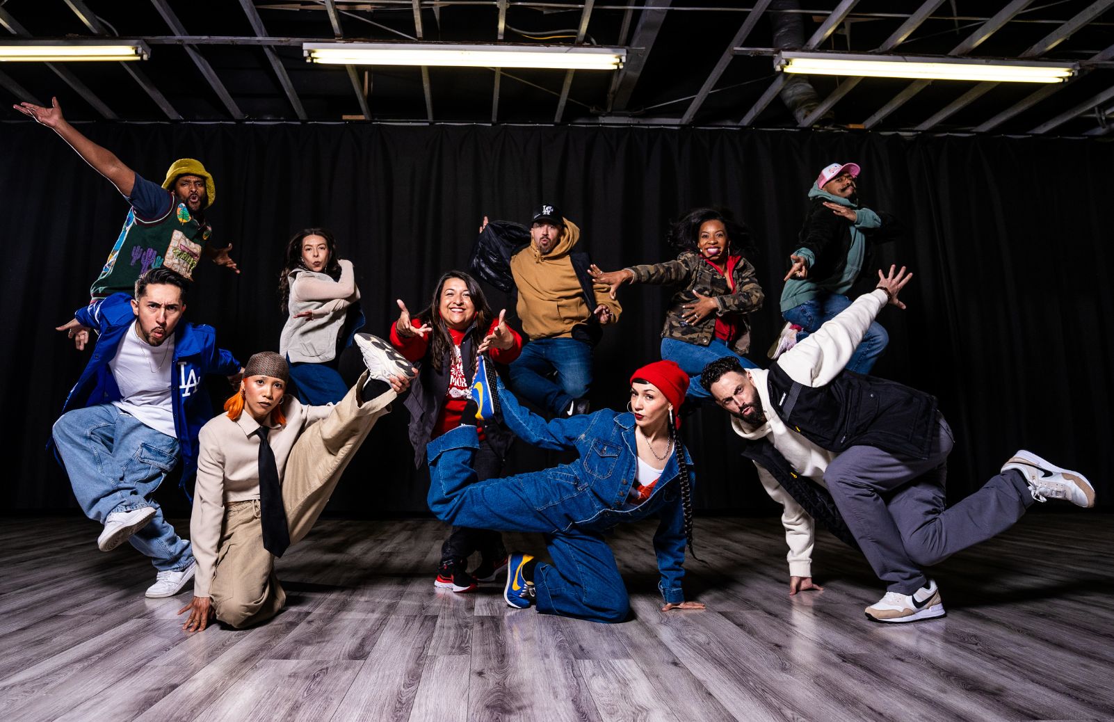 A street dance ensemble strikes dynamic poses together in a rehearsal studio.