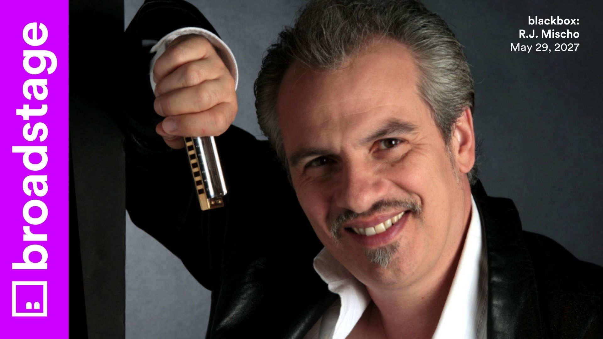 A man with white hair smiles in front of a grey background. He's wearing a suit and holding a harmonica. There are purple graphics that say "BroadStage" and "blackbox: R.J. Mischo May 29, 2027"