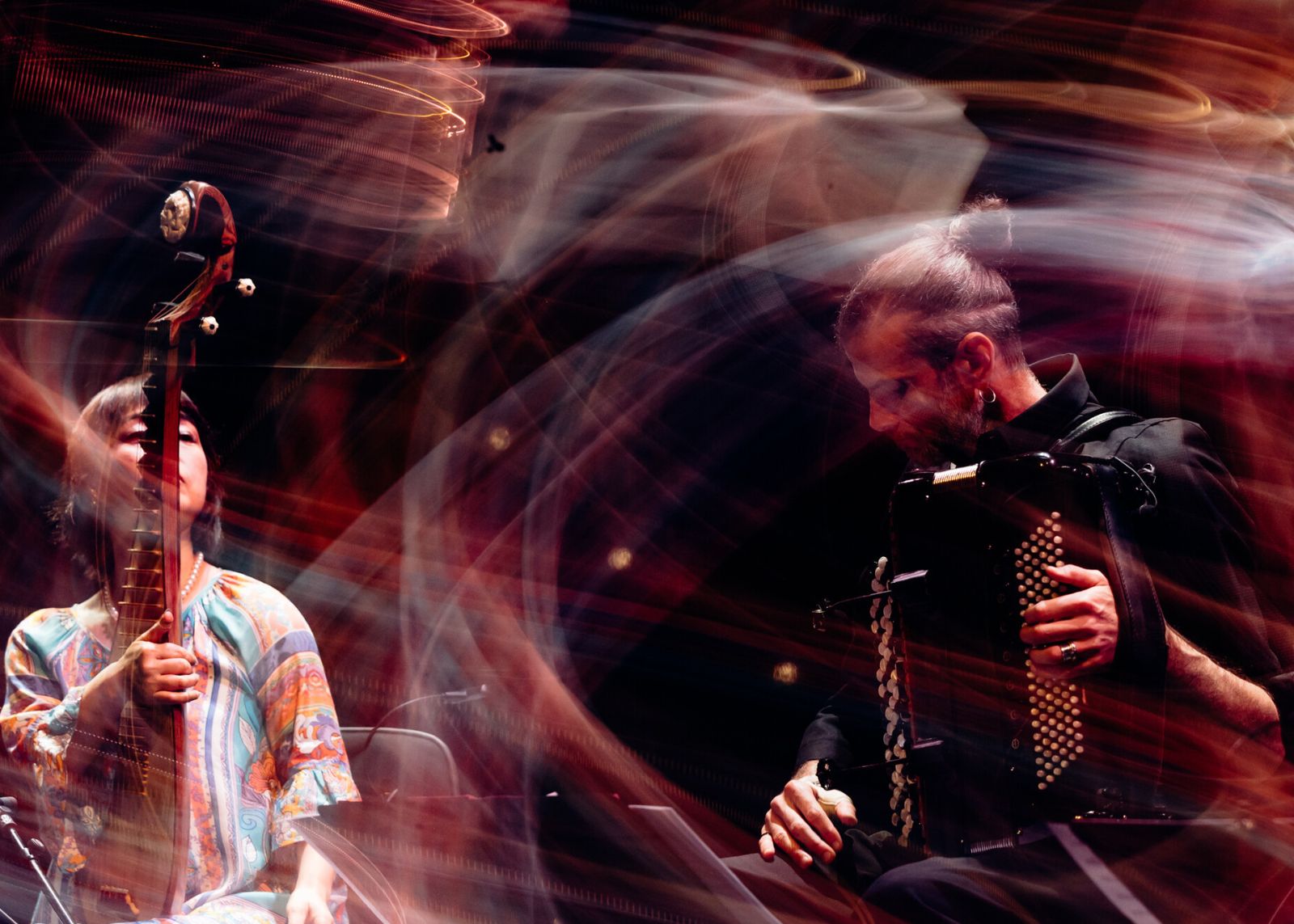 A pipa player and an accordionist perform together, enveloped in sweeping red and gold light trails.