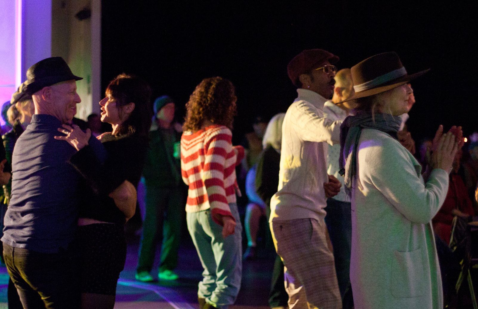 Audience members dance together at an outdoor blackbox event under colorful lighting.