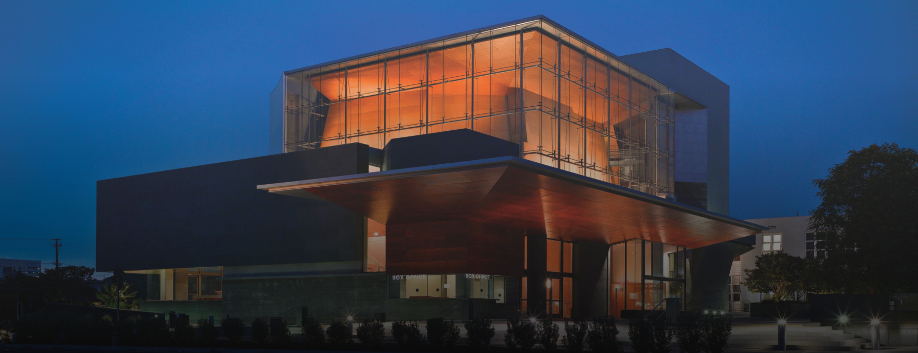BroadStage building at dusk, its glass upper level glowing amber against a deep blue sky.