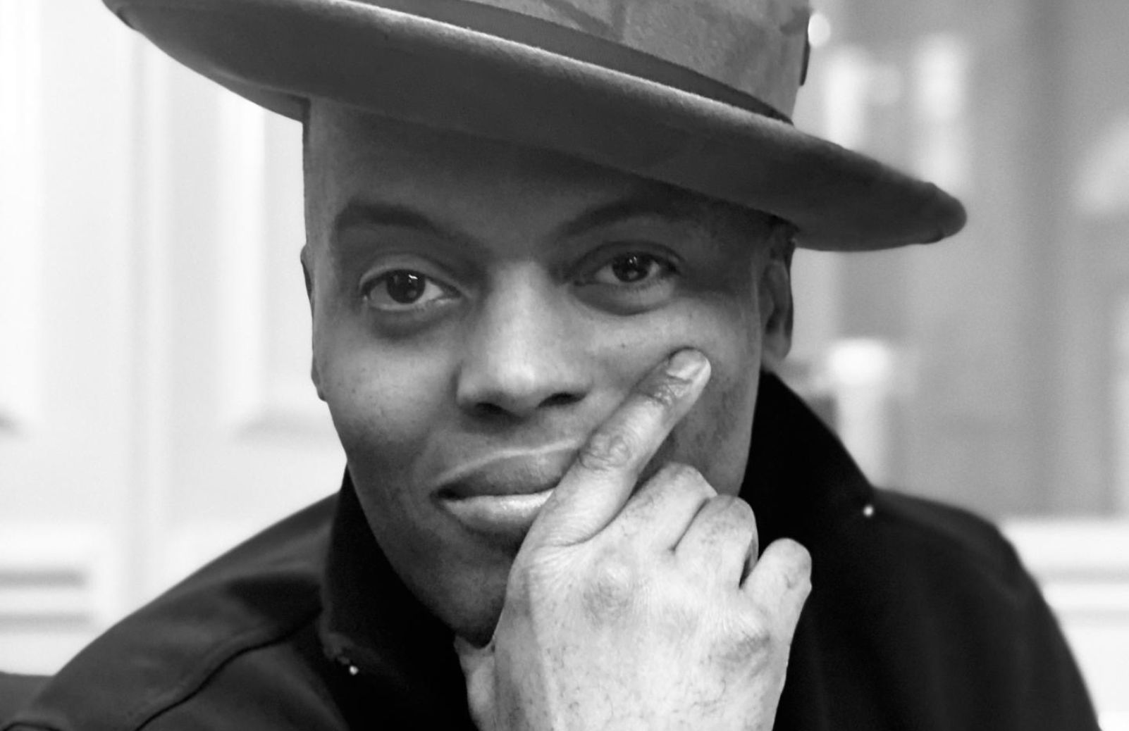 Black and white portrait of a man in a wide-brim hat, resting his chin on his hand.