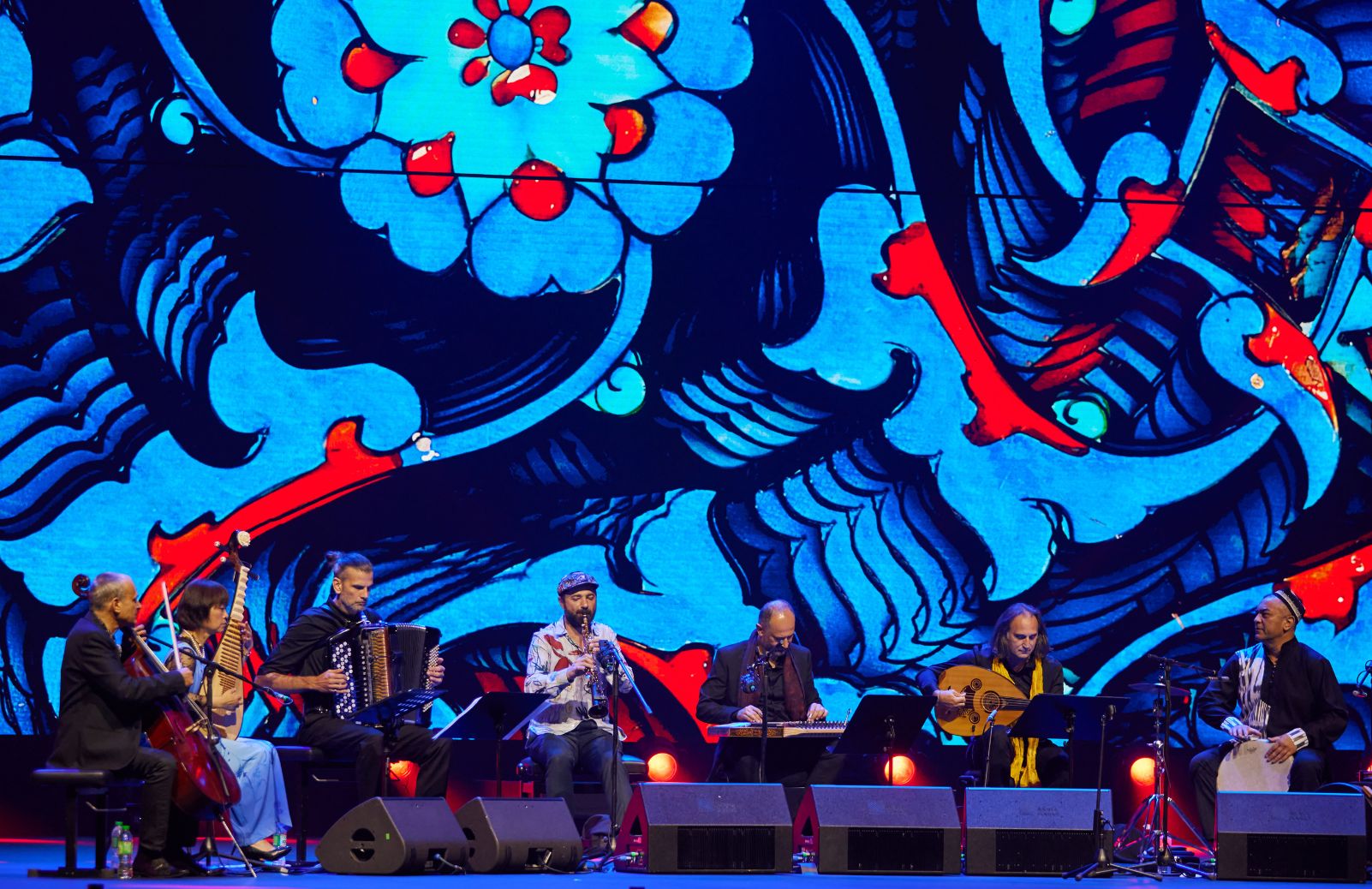 A music ensemble plays in front of a vibrant blue and red backdrop.