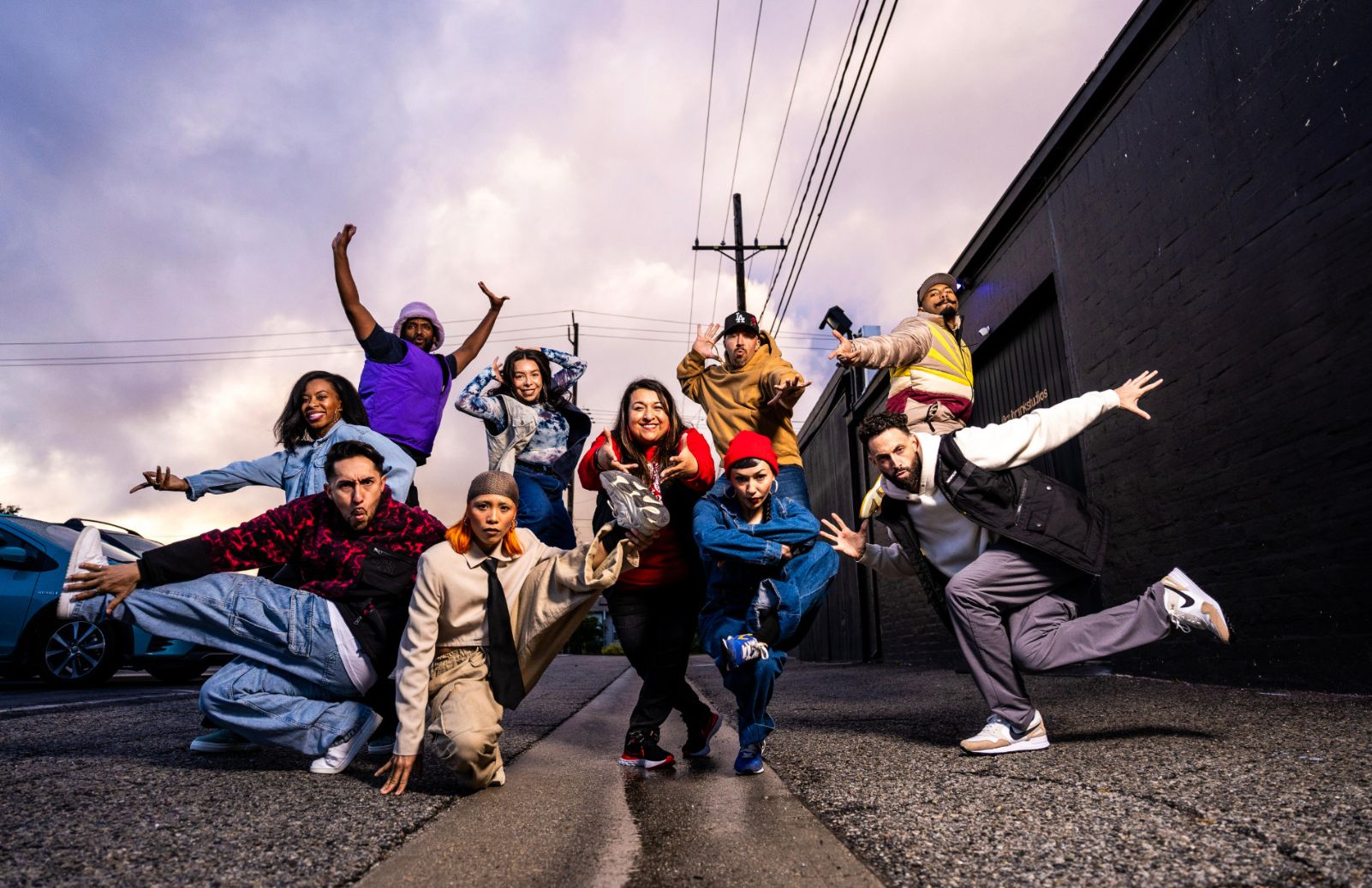 A street dance ensemble strikes dynamic poses together outside.