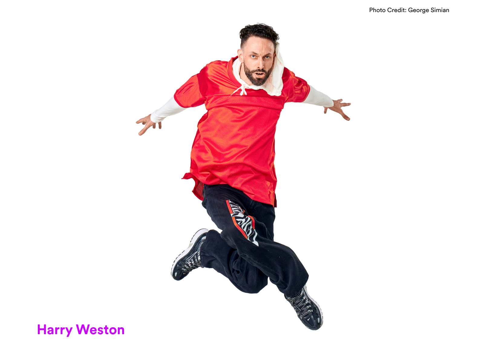 Dancer Harry Weston jumps with arms outstretched and an intense expression, wearing a red mesh jersey over a white long-sleeve. Photo: George Simian.