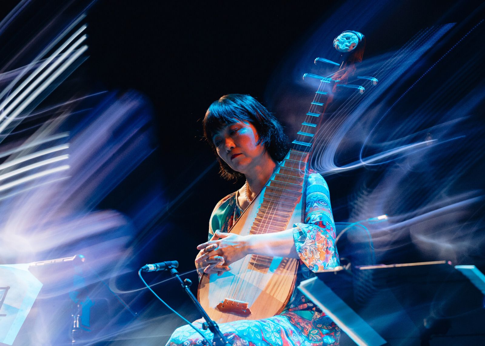 A pipa player performs, surrounded by swirling blue light trails on a dark stage.