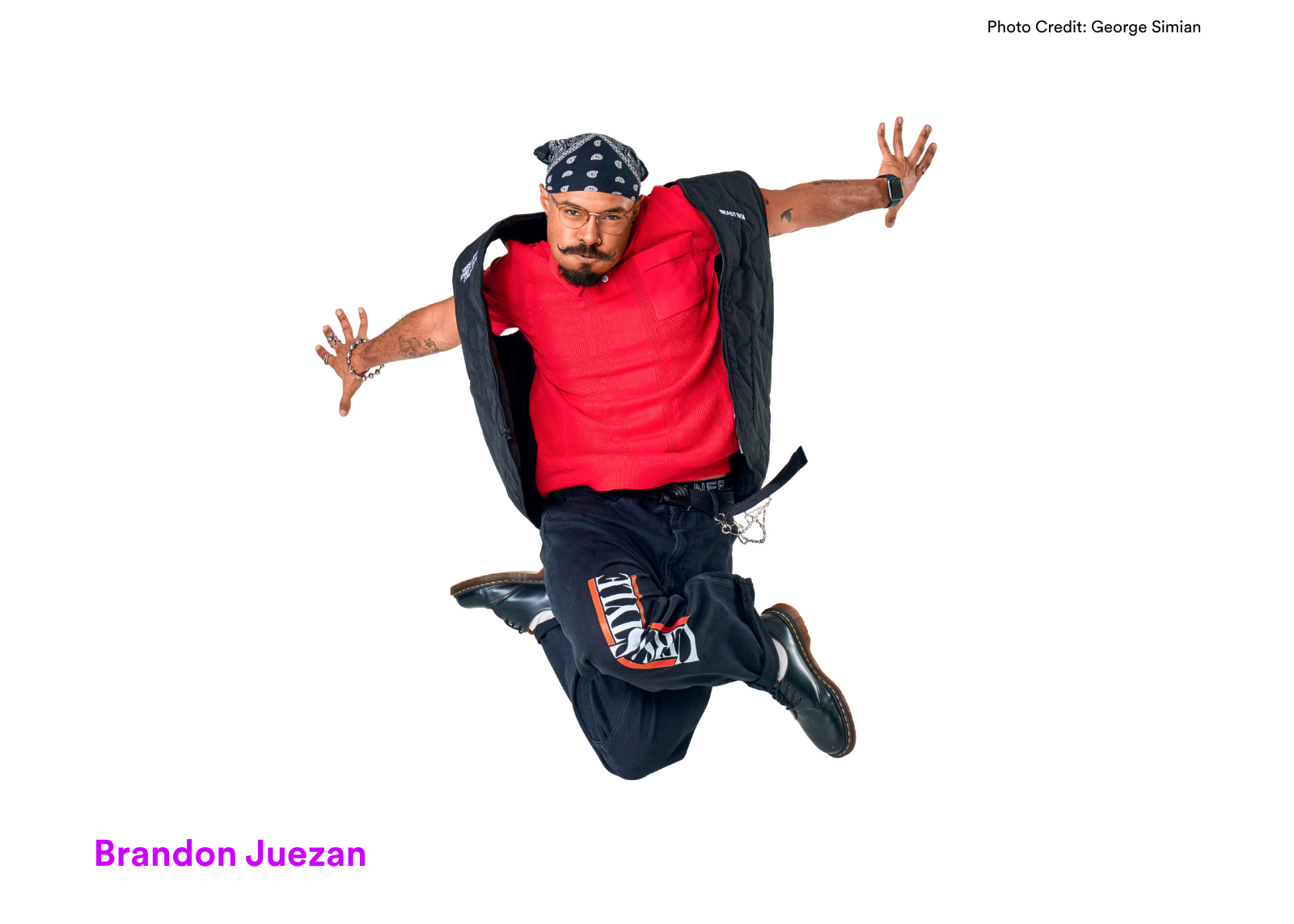 Dancer Brandon Juezan jumps mid-air with arms spread wide, wearing a red top, black vest, and bandana headscarf. Photo: George Simian.