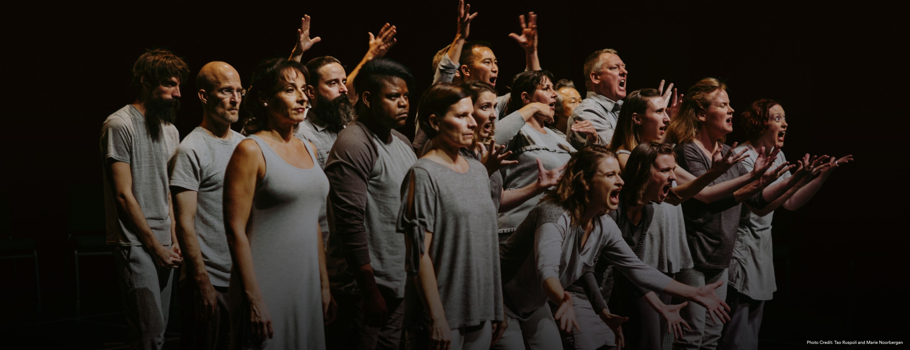 A group of people all wearing grey make exasperated expressions onstage.
